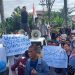 Protes kebijakan Wali Kota Kotamobagu Tatong Bara datang dari para pedagang kaki lima bersama, aktifis LSM dan elemen masyarakat Kota Kotamobagu. Mereka menggelar aksi demo di Kantor DPRD dan Kantor Kejaksaan Negeri Kotamobagu Senin 8 Agustus 2022. Aksi itu untuk memprotes kebijakan Wali Kota Tatong Bara yang dinilai merugikan masyarakat dan pedagang. Aksi demo ratusan massa itu, diawali di depan Kantor Kejaksaan. Kedatangan mereka untuk memberikan dukungan sekaligus mendesak agar pihak Kejaksaan menseriusi kasus dugaan Korupsi Pasar Genggulang yang sedang ditangani. Kasus korupsi Pasar Genggulang telah menetapkan dua orang sebagai tersangka. Salah satu peserta aksi, dari elemen masyarakat Irawan Damopolii mengatakan, aksi yang digelar tersebut bertujuan untuk menyampaikan dukungan sekaligus meminta agar Kejaksaan serius. "Aksi ini sebagai wujud dukungan kami, agar Kejaksaan seriusi dalam penanganan kasus korupsi Pasar Genggunlang yang telah menetapkan dua orang sebagai tersangka," kara Irawan. Menurutnya, proyek pembangunan Pasar Genggulang yang menggunakan APBD puluhan miliaran rupiah itu, telah merugikan masyarakat sehingga perlu diseriusi. Selama kurang lebih 30 menit berorasi di depan Kantor Kejaksaan, masa melanjutkan melakukan aksi di depan Kantor DPRD di Jalan Paloko Kinalang. Saat tiba di depan Kantor DPRD sempat terjadi aksi dorong dengan petugas karena massa memaksa masuk. Namun aksi dorong itu tak berlangsung lama karena Ketua DPRD Kotamobagu Meiddy Makalalag langsung menemui massa pendemo dan mempersilahkan masuk. Di hadapan para wakil rakyat, mereka menyampaikan aspirasi, terkait kebijakan Wali Kota Kotamobagu yang menutup akses masuk di Pasar Serasi dan jalan 23 Maret. Penutupan akses ke pasar itu, melibatkan aparat dari TNI POLRI. Sedikitnya ada empat titik akses yang diblokade dan jaga ketat aparat. Penutupan itu, buntut pemindahan sebagian pedagang ke Pasar Genggulang. Menurut mereka, keijakan tersebut justru merugikan para pedagang serta pemilik toko lainnya. “Kebijakan Wali Kota Kotamobagu Tatong Bara yang menutup akses jalan masuk ke pasar Serasi tidak manusiawi dan hanya merugikan masyarakat yang tinggal di kompleks pasar. Begitu juga bagi para pedagang warung makan dan toko penjual bahan bangunan,” kata Ketua salah satu elemen masyarakat Ando Lobud. Ando menegaskan, penutupan beberapa titik masuk ke Pasar Serasi telah melanggar hak asasi manusia sebab banyak warga yang merasa tertekan dan pedagang dirugikan. "Kami sebagai warga yang tinggal di kompleks Pasar Serasi dan Pasar 23 Maret menerima dampak dari penutupan akses masuk. Selain itu, ikut memberikan kerugian bagi para pemilik warung makan, toko, dan kios," katanya. Dibeberapa titik masuk ke Pasar Serasi dan Pasar 23 Maret sejumlah aparat TNI Polri ikut dikerahkan untuk berjaga-jaga. Padahal hanya dalam rangka memindahkan sebagian pedagang ke Pasar Genggulang karena telah menempati badan jalan. "Di Kompleks pasar itu, bukan hanya pedagang kecil saja yang berjualan. Tetapi di sana ada toko, dan warung makan. Selama penutupan jalan, para pemilik warung makan mengalmi kerugian karena tidak ada pembeli," katanya. Ketua LBI Dofie Paat lewat pernyataan sikap menegaskan, menolak penutupan jalan keluar masuk pasar yang dilakukan Pemkot Kotamobagu sejak Kamis (4/8). Menurut Dolfie, penutupan akses ke pasar seperti Daerah Operasi Militer (DOM) dan mencekam. Karena disetiap pos penjagaan ada aparat terkesan di wilayah itu terkesan seperti ada Teroris Pusat perbelanjaan usaha pertokoan,rumah makan, serta transportasi mati total karna tidak bisa masuk.Dan ini telah mengakibatkan pelaku usaha rugi besar. “Selaku Ormas, kami meminta kepada DPRD membuat rekomendasi untuk segera membuka akses,” tegasnya. Ketua DPRD Kotamobagu Meiddy Makalalag berjanji akan turun untuk melihat secara langsung penutupan akses masuk pasar. (*)