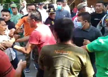 TOTABUAN.CO KOTAMOBAGU – Proyek pemagaran akses jalan masuk Rumah Sakit Umum Daerah Kotamobagu berujung ricuh Jumat 4 November 2022. Akibatnya warga yang menolak proyek pemagaran tersebut terlibat saling dorong dengan petugas dari Satpol PP. Para pekerja proyek pemagaran akses jalan masuk RSUD Kotamobagu itu dihalangi warga dengan membuat garis batas pagar dengan menggunakan alat berat. Namun aksi tersebut dicegat petugas Satpol PP. Aksi saling dorong pun terhindarkan karena warga berupaya menghentikan proses pekerjaan yang sedang berlangsung. Akibatnya, salah satu ibu jatuh pingsan sehingga harus dilarikan ke rumah sakit untuk mendapatkan pertolongan medis. Menurut warga aksi penolakan ini sebagai bentuk protes terhadap kebijakan pemerintah Kotamobagu yang melakukan pemagaran jalan masuk RSUD Kotamobagu setinggi dua meter perlu dikaji kembali. Sebab akan berdampak pada usaha warga seperti warung, kios dan rumah makan tempat mereka mencari nafkah sehari-hari. “Jalan ini milik publik semua orang punya hak menggunakan jalan ini baik pejalan kaki maupun kendaraan. Jangan sampai pemagaran ini merampas hak masyarakat. Pemerintah harus arif dan bijaksana. Ini kesalahan prosedural apalagi dalam pekerjaan ini melibatkan TNI," ujar Rofinus Talulendang. Penolakan itu lantaran Pemkot Kotamobagu dinilai melanggar kesepakatan awal yang notabene tidak ada pemagaran ruas jalan. Kendat demikian, pemerintah punya alasan terkait pemagaran tersebut. Selain untuk meningkatkan akreditas rumah sakit rujukan di Bolaang Mongondow Raya, pihak rumah sakit juga telah melakukan sosialisasi kepada warga sekitar. Bahkan akses tetap diberikan kiri dan kanan selebar 3,5 meter. "Dasar pemagaran ini sesuai dengan Permenkes Nomor 14 Tahun 2021 terkait akses jalan masuk rumah sakit. Kami juga jauh sebelumnya telah mensosialisasikan terkait pemagaran ini. Bahkan tetap akan berikan jalan. Pemagaran ini dilakukan untuk akreditas rumah sakit karena rumah sakit Kotamobagu merupakan rumah sakit rujukan di BMR," ujar Kabag Umum dan Adminitrasi RSUD Kotamobagu Topan Simbala. Kendati mendapat penolakan dari warga, proses pekerjaan tetap berlangsung. Diketahui pada pelaksana pekerjaan itu dilakukan lewat Karya Bhakti oleh Kodim 1303 Bolaang Mongondow dengan total anggaran senilai  900 juta rupiah. (*)